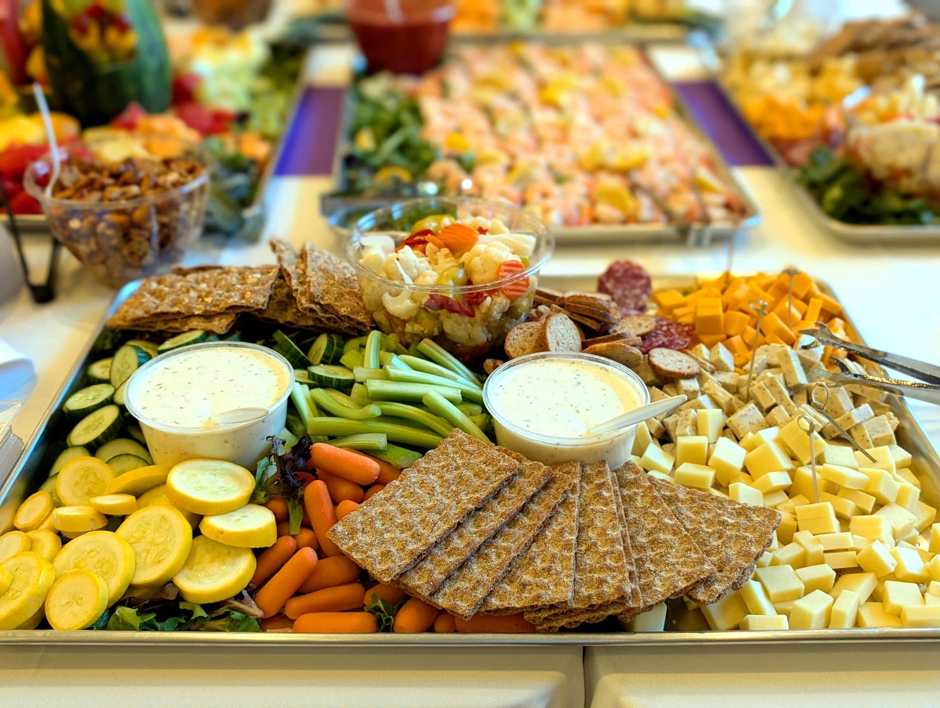 Catering spread with fresh vegetables, cheeses, crackers, and dips